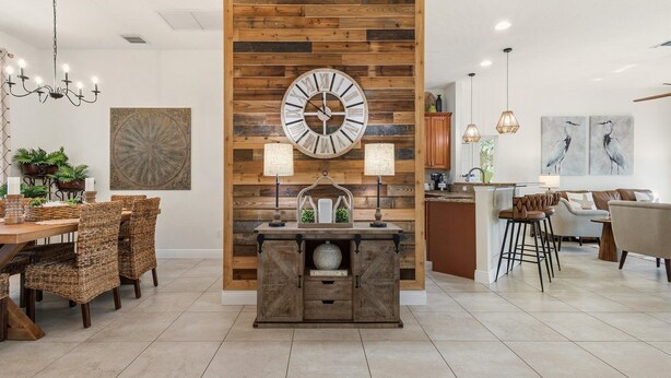 A modern kitchen with a wooden accent wall, a large clock, and a bar area with stools. - Premium Modern Pool Home- 1 Mile to Downtown & 3 Miles to Beaches (Jensen Beach)