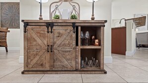 A wooden cabinet with a rustic design, featuring two doors and a shelf with glassware and copper pots. - Premium Modern Pool Home- 1 Mile to Downtown & 3 Miles to Beaches (Jensen Beach)