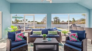 A covered patio area with wicker furniture, cushions, and a small table. - Premium Modern Pool Home- 1 Mile to Downtown & 3 Miles to Beaches (Jensen Beach)