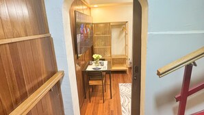 Un pasillo con puerta de madera, una pequeña mesa con sillas y suelo de baldosas.
