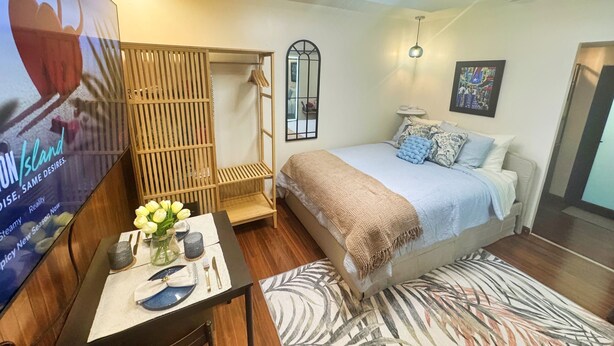Un dormitorio con cama, una mesita de noche con un jarrón de flores, un armario de madera, un espejo y una lámpara en el techo.
