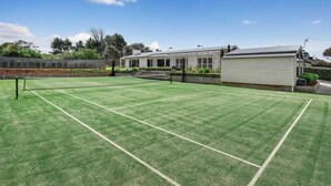 Un court de tennis avec un filet, entouré d’une clôture, et un petit abri de jardin.