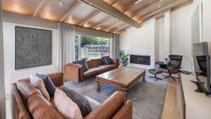 Un salon spacieux avec un haut plafond, une cheminée, des canapés en cuir, une table basse et un téléviseur.