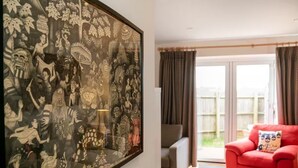 Een kamer met een groot kunstwerk in een lijst aan de muur, een rode bank en uitzicht door een glazen deur.