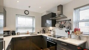 Een moderne keuken met donkere kastjes, een roestvrijstalen afzuigkap en een raam met zonwering.
