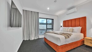 Une chambre d’hôtel moderne dotée d’un grand lit, d’un téléviseur fixé au mur, d’une fenêtre avec des rideaux et d’un appareil de climatisation.
