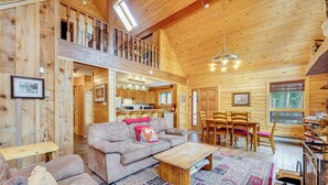 Une cabane en bois spacieuse avec une chambre à coucher en mezzanine, un coin salon confortable avec un canapé et une table basse, et un coin repas avec des chaises.