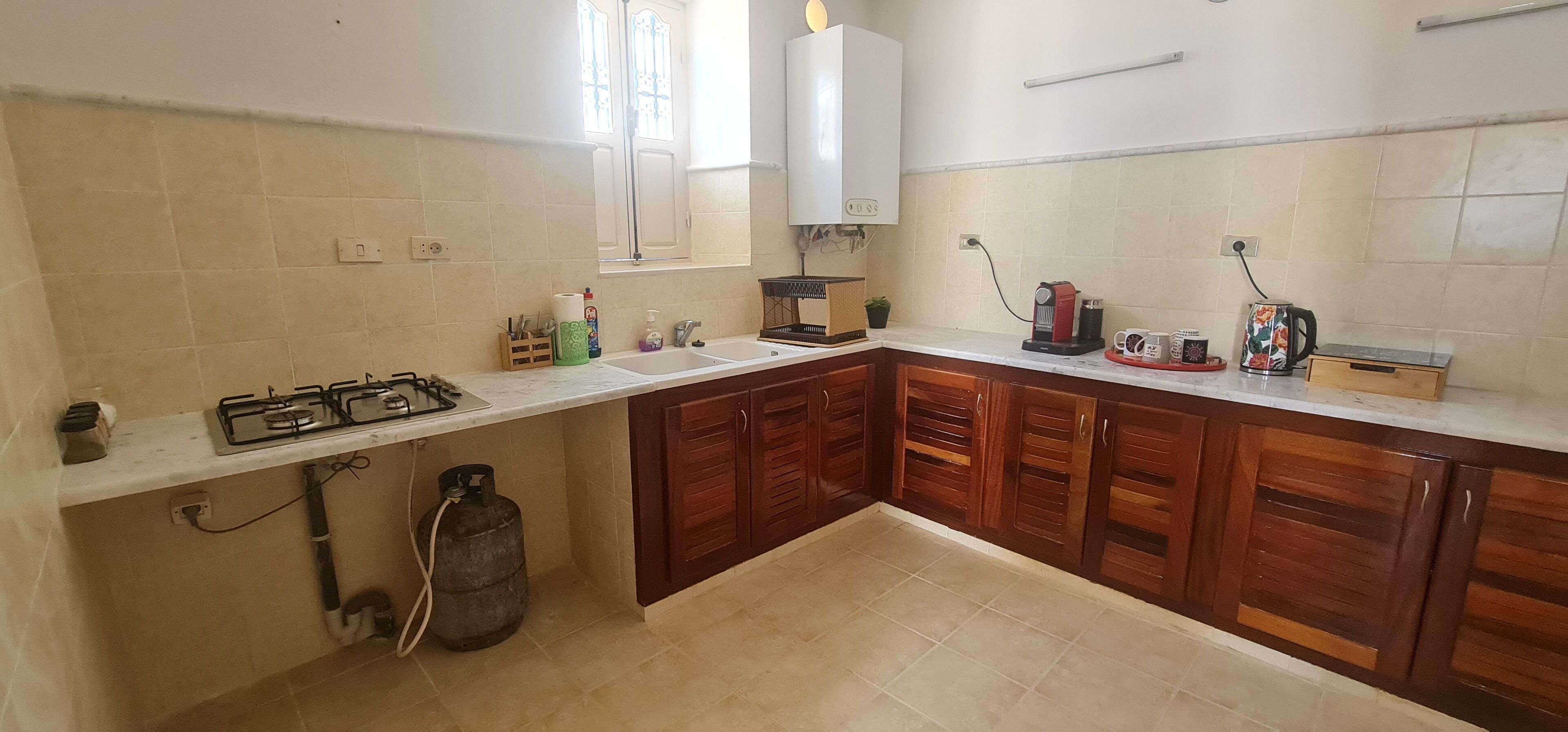 Una cucina con un piano cottura a gas, una bombola di gas, mobili in legno, una finestra e un ventilatore a soffitto bianco.