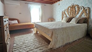 A bedroom with a wooden ceiling, a bed with a patterned headboard, a sofa, and a small wooden table. - Beit El Ezz Kerkennah  (Kerkennah Islands)