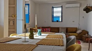 A room with a bed, a table with a vase, a sofa, and a window with bars. - Beit El Ezz Kerkennah  (Kerkennah Islands)