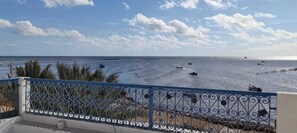 A coastal view with a metal railing, palm trees, and boats on the water. - Beit El Ezz Kerkennah  (Kerkennah Islands)