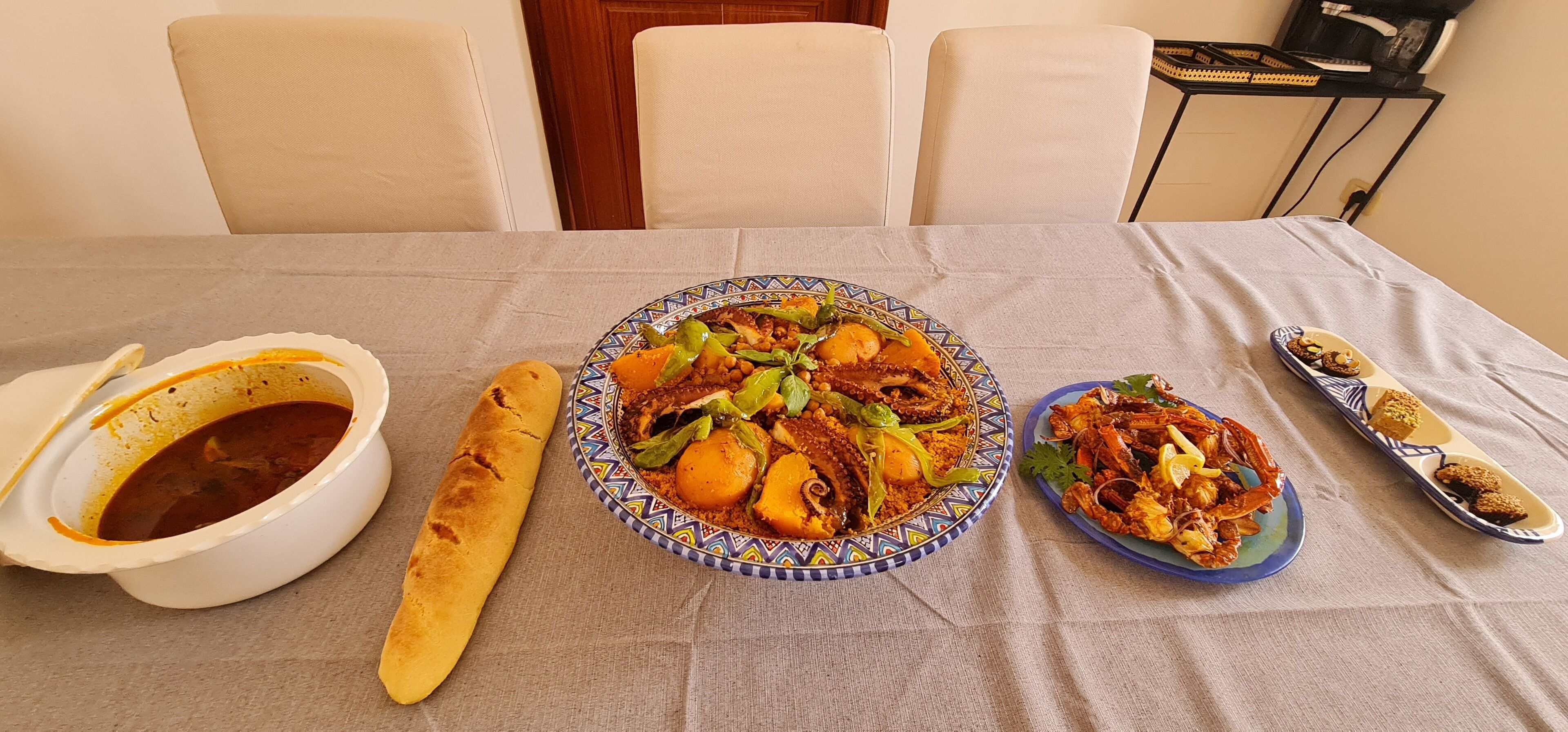Een gedekte tafel met een maaltijd, inclusief een kom soep, een brood, een bord stoofpot en een bord zeevruchten.