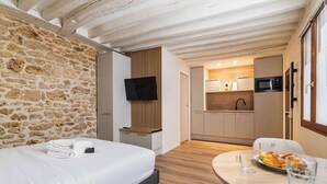 Una camera da letto con un letto, una TV a schermo piatto, una parete in legno, una cucina con un forno a microonde e un'area pranzo con tavolo e sedie.