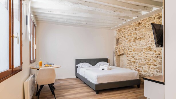 Una camera da letto con un letto, un tavolino con una sedia, un termosifone e un muro in pietra.