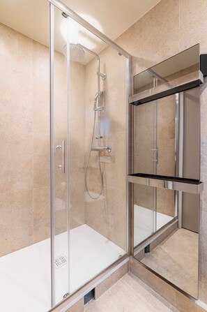 A modern shower enclosure with a glass door, a handheld showerhead, and a wall-mounted control panel.