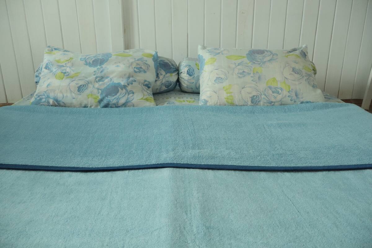 A bed with a blue blanket and floral-patterned pillows against a white wall.