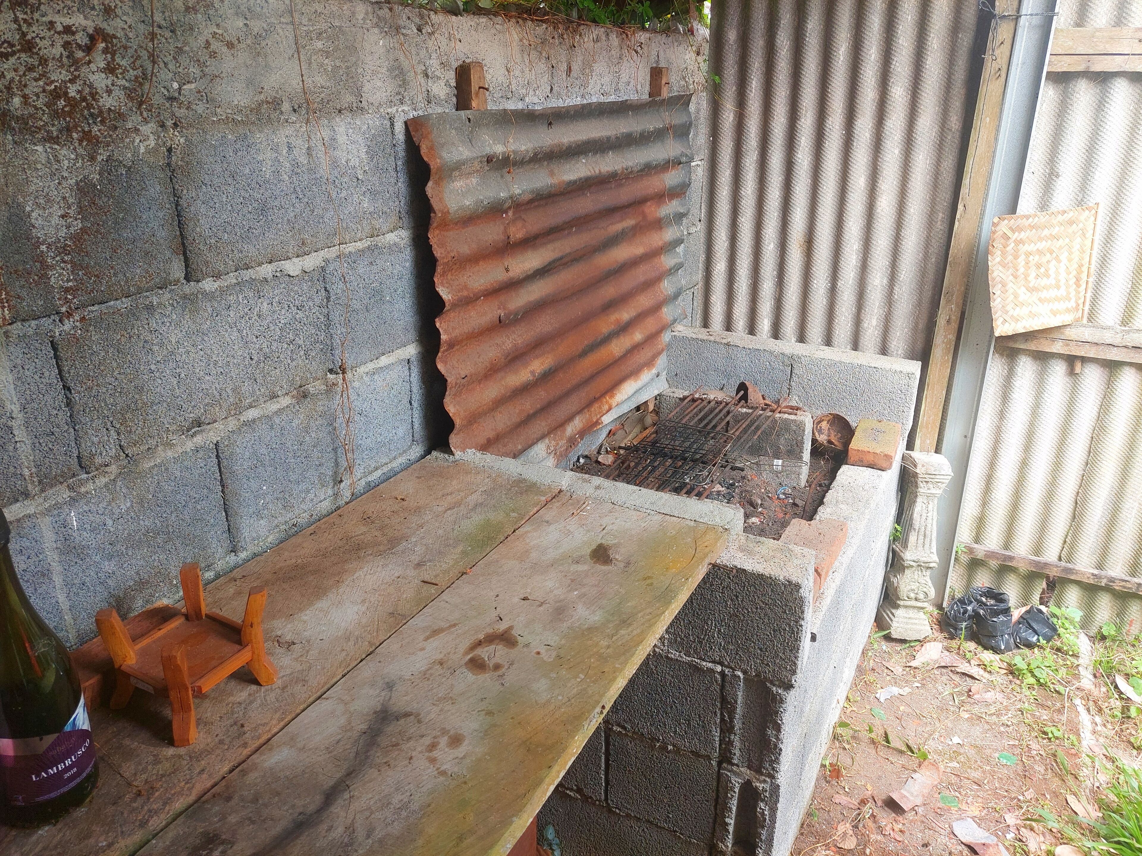 Een rustieke buitenruimte met een houten bank en een metalen barbecue.