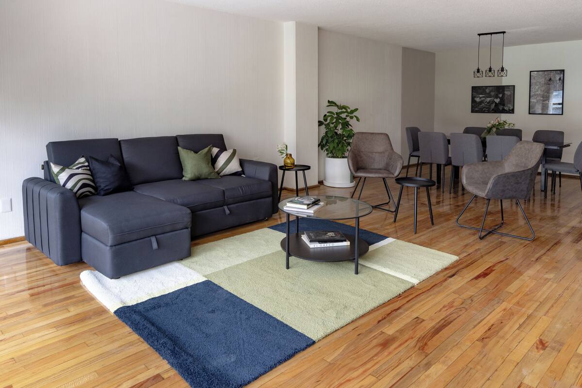 Una sala de estar moderna con un sofá gris, una mesita de centro y un comedor con sillas grises.