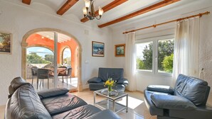 A living room with leather sofas, a glass coffee table, and a view of the outdoors through large windows. - Ker Blanc 8 pax - Javea, Costa Blanca (Javea)