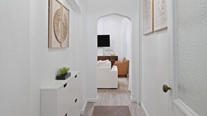 Un couloir avec une commode blanche, une plante et des œuvres d’art encadrées accrochées au mur.
