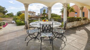 An outdoor patio with a round table and chairs, surrounded by columns and a view of buildings and greenery.