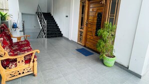 Tilava eteinen, jossa on puinen portaikko, koristeellinen puuovi, ruukussa oleva kasvi ja punaisella kankaalla verhoiltu penkki.