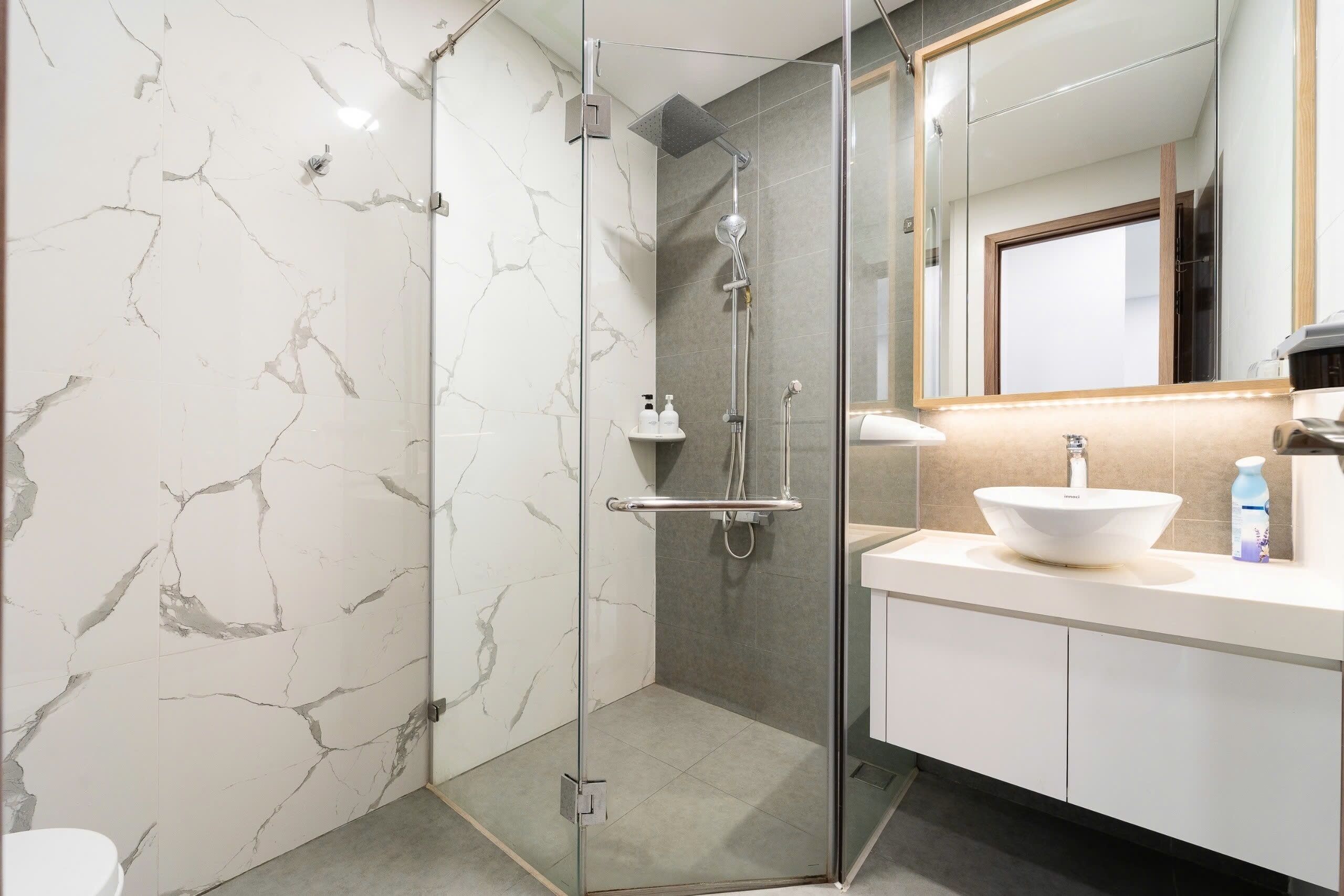 A modern bathroom with a glass-enclosed shower, a white sink, and marble walls.