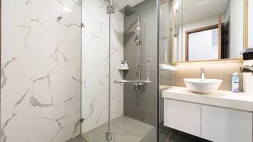 A modern bathroom with a glass-enclosed shower, a white sink, and marble walls.