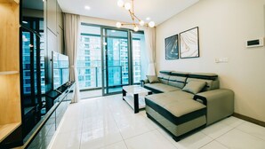 A modern living room with a sofa, a coffee table, and a TV. There is a large window with a view of buildings. - Sunwah Pearl Suites  (Ho Chi Minh City)