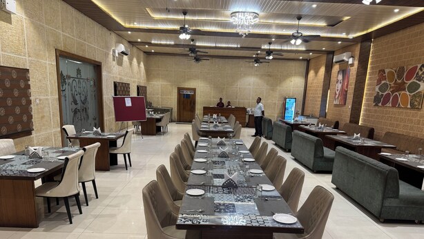 A spacious restaurant with long tables, cushioned chairs, and a modern ceiling design. -  Meera Resort- Korba (Korba)
