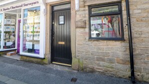 A stone building with a black door and a window displaying a statue. - Cosy Cottage (Buxton)
