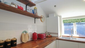 A kitchen with wooden countertops, a red kettle, a toaster, and a clock on the wall. - Cosy Cottage (Buxton)