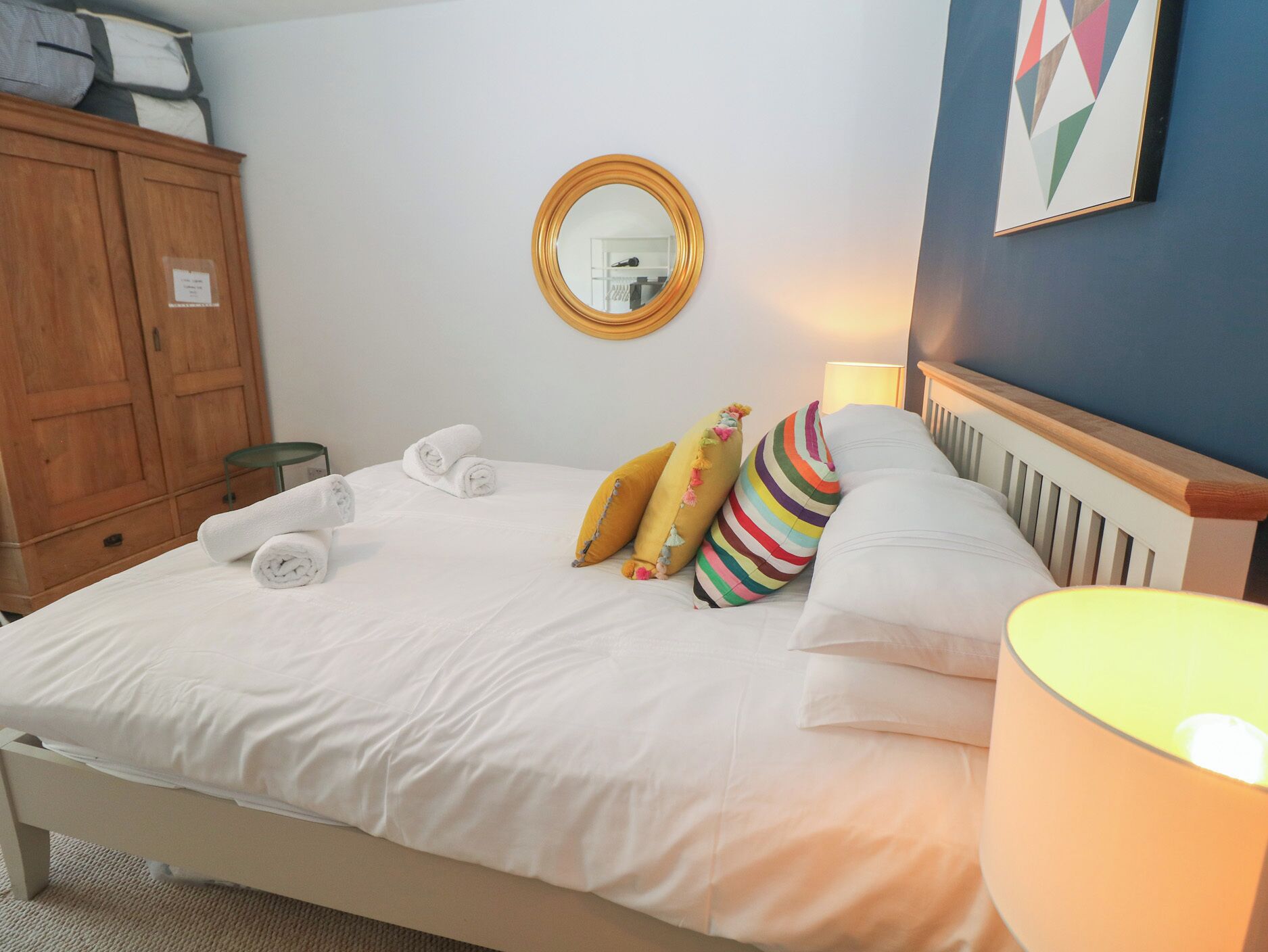 Un lit bien fait, avec des serviettes pliées en rouleaux, une lampe de chevet et des coussins aux couleurs vives.
