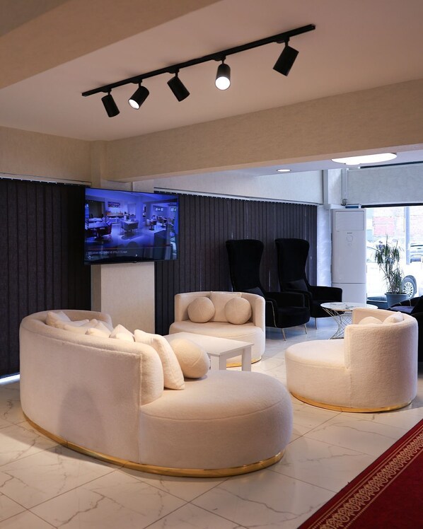 Een moderne woonkamer met een bank, fauteuils en een salontafel. Er is een flatscreen televisie aan de muur bevestigd, en de kamer heeft een groot raam.