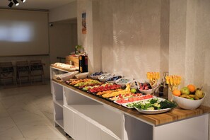 A buffet with various fruits and vegetables, a white cabinet, and a projector screen in the background. - Başaran Rezidans & Otel (Malatya)