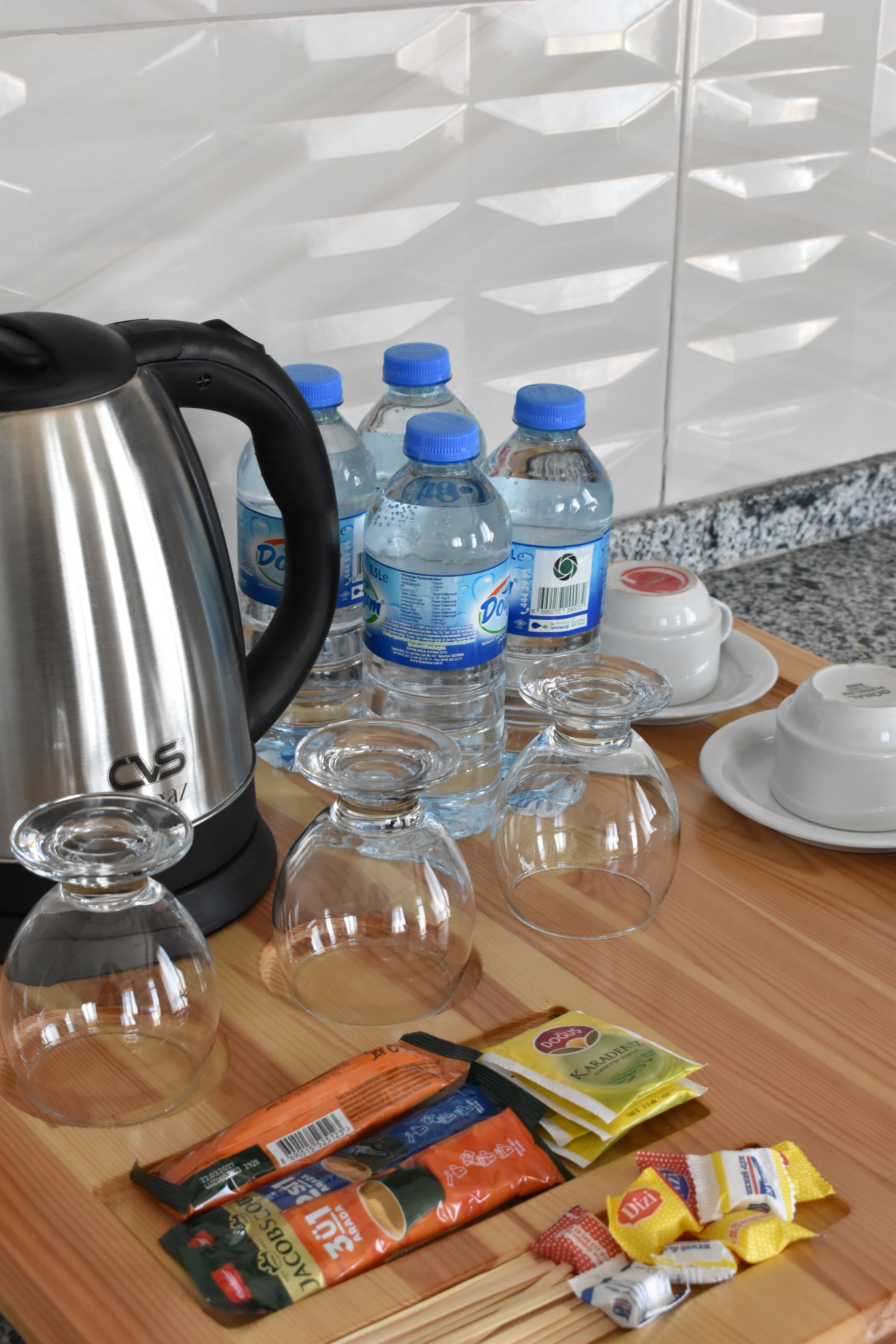A kitchen counter with a kettle, water bottles, glass tumblers, and packaged snacks.