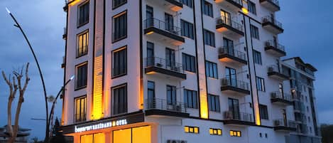 A multi-story hotel with balconies, a ground-level restaurant, and a parking area.