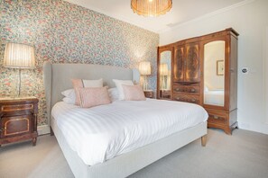 Ein Schlafzimmer mit einem großen Bett, zwei Nachttischen mit Lampen, einem Holzschrank und blumigem Wandpapier.