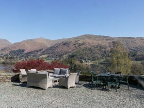 Eine Terrasse mit Korbmöbeln und einem Tisch, mit Blick auf einen See und Berge.