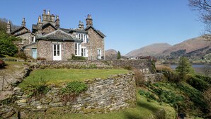 A stone house with a stone wall in front, a grassy yard, and a lake in the background. - Huntingstile South (Ambleside)