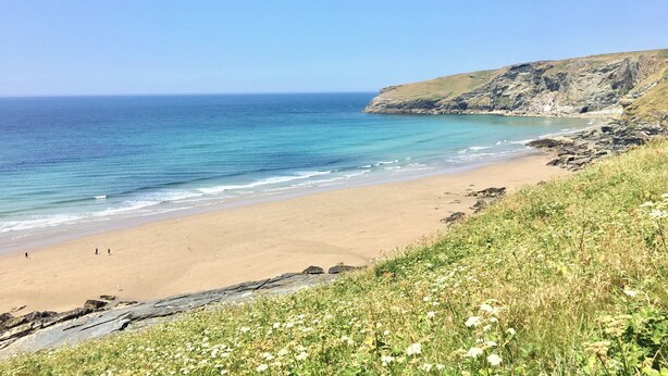 A coastal beach with clear blue water, sandy shore, and rocky cliffs. - Mews Cottage (Tintagel)