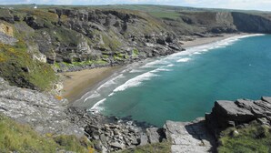 A coastal landscape with rocky cliffs, a beach, and a clear blue sea. - Mews Cottage (Tintagel)