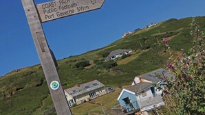 A wooden signpost indicating the Coast Path Public Footpath to Port Gavene, 5½m away. - Mews Cottage (Tintagel)