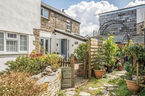 Een stenen vakantiehuisje met een witte gevel, een houten poort en een tuin met bloempotten.