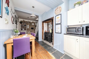 A kitchen with a stone wall, wooden flooring, a dining table with chairs, and a microwave. - Mews Cottage (Tintagel)