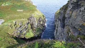 A coastal landscape with rocky cliffs and a narrow sea passage. - Mews Cottage (Tintagel)