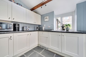 A kitchen with white cabinets, a microwave, a toaster, and a coffee maker. - Mews Cottage (Tintagel)