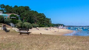 Une plage avec un banc en bois, un vélo et une maison en arrière-plan.