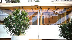 Un espace extérieur moderne doté d’une terrasse en bois, de deux grands pots de plantes et d’un coin salon abrité offrant une vue sur un paysage montagneux.