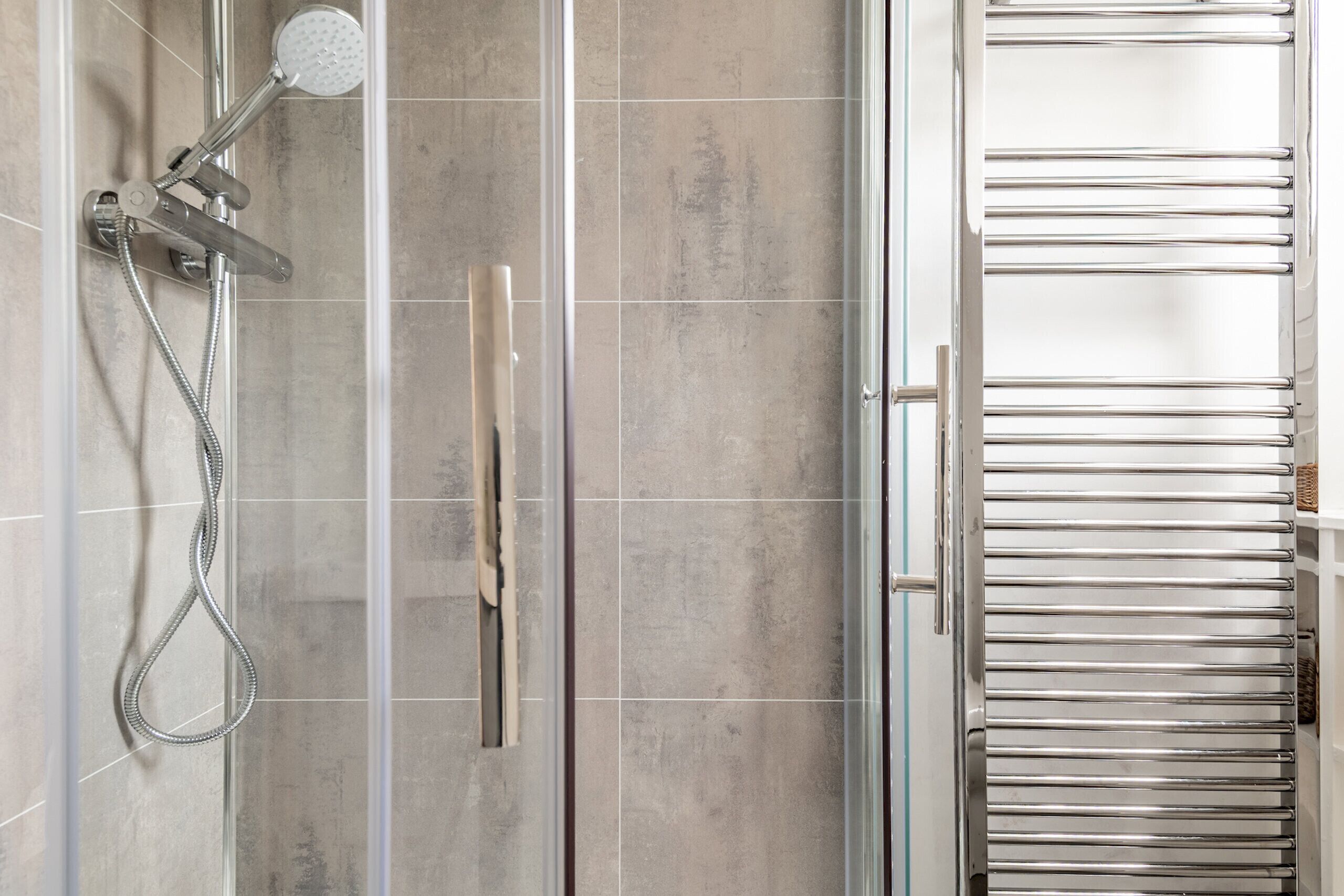 A bathroom with a glass shower enclosure, a towel rack, and a glass door.